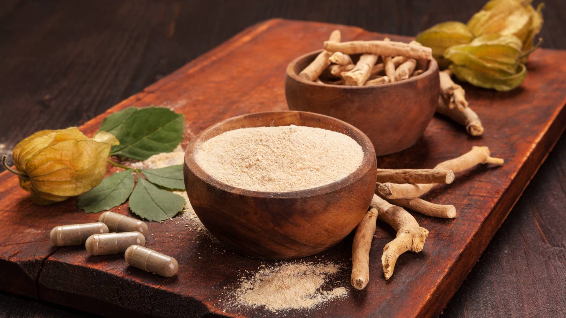 Ashwagandha rohtokoiso hyodyt Ashwagandhajauhetta puukulhossa, ashwagandhajuuri pöydällä